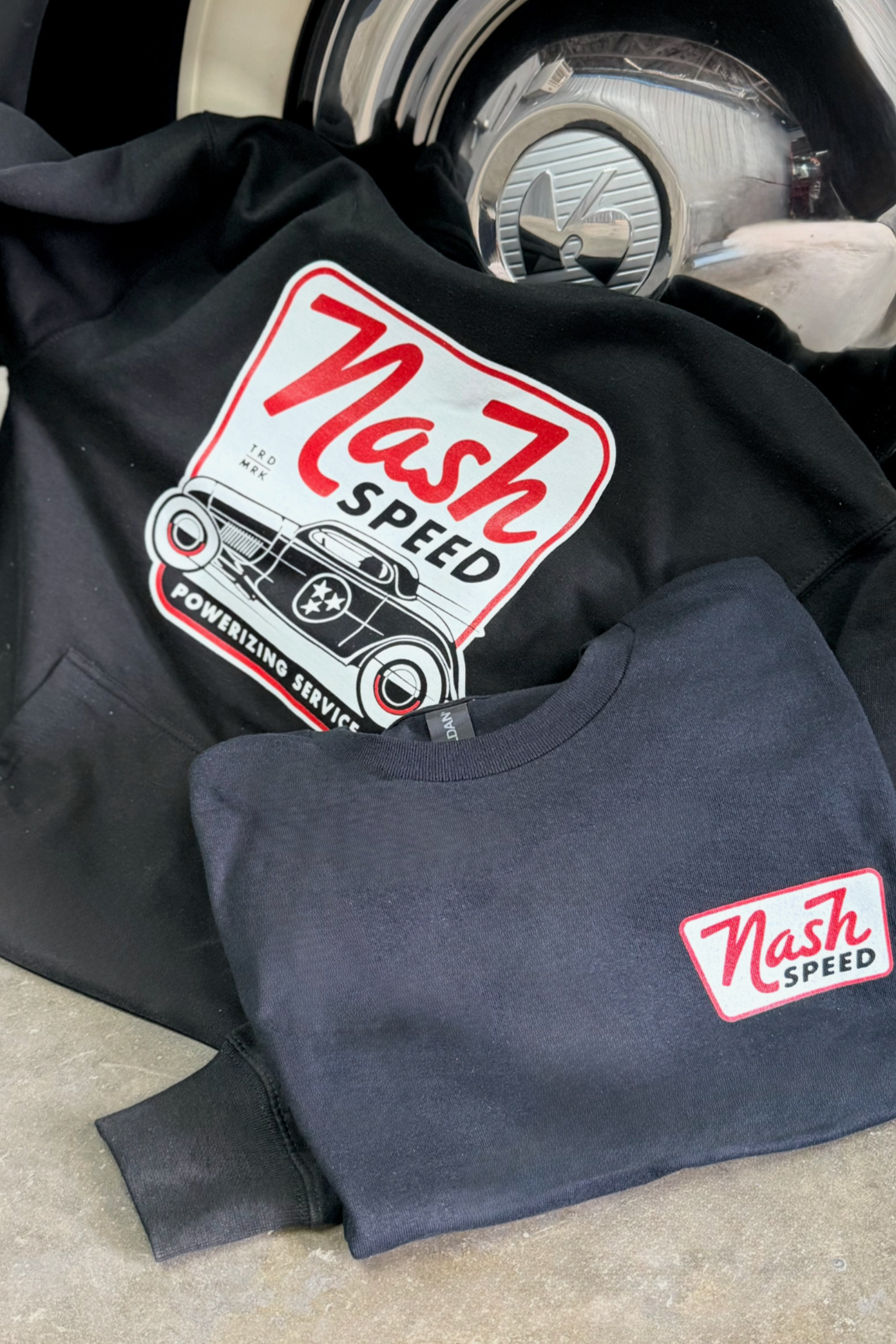 Two sweatshirts with 'Nash Speed' logo resting on a car tire